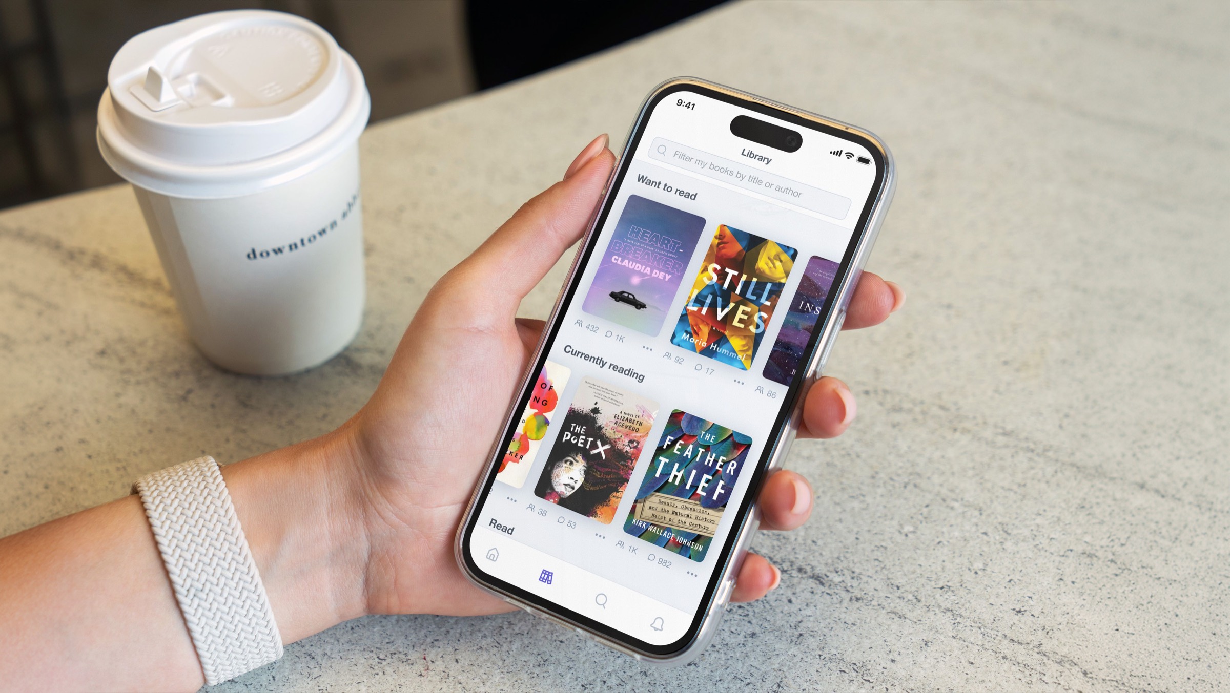 Eine Hand hält ein Telefon mit einer Byzans-Bibliothek voller Buchcover, neben einer Kaffeetasse