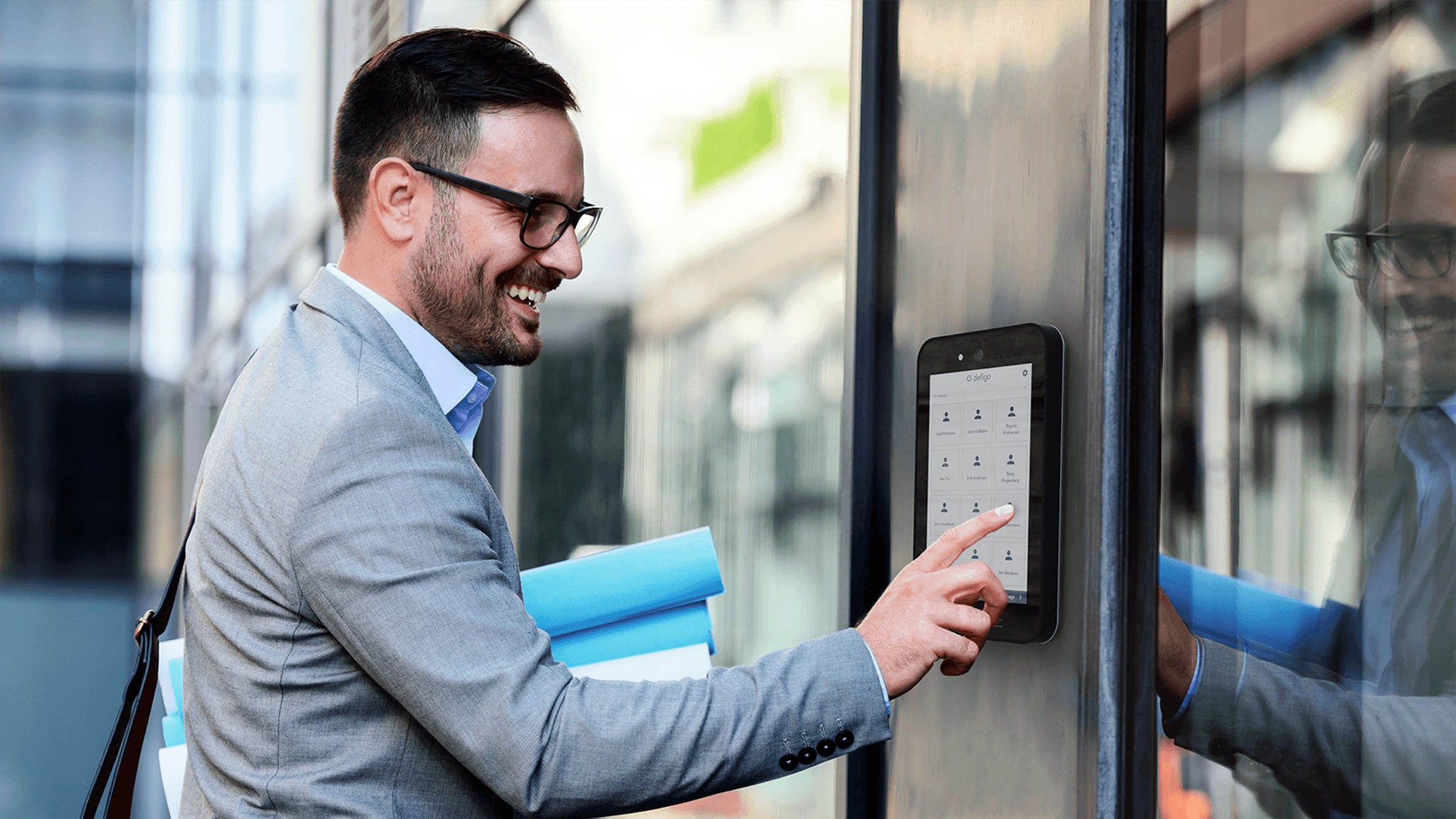 Ein lächelnder Mann tippt am Gebäudeeingang auf den Bildschirm der smarten Defigo-Türsprechanlage